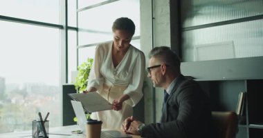 Bir iş kadını modern ofis ortamında bir iş adamına bir belge sunar. İşbirlikçi bir toplantıda finansal verileri ya da analizleri tartışıyor gibi görünüyorlar..