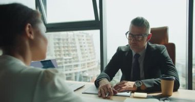 Profesyonel iş adamı, modern bir gökdelendeki toplantıda meslektaşıyla fikir ve stratejilerini paylaşıyor ve el hareketleriyle amacını vurguluyor..