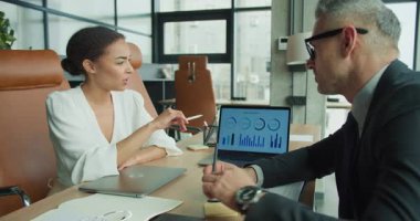 İş kadını ve işadamı, modaya uygun, modern bir ofis ortamındaki toplantı sırasında dizüstü bilgisayarlarında analitiği bilgi tablosuyla tartışıyor..