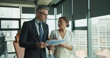 Modern bir ofiste çalışan bir işadamı ve iş kadını, finansal verileri kağıt üzerinde gözden geçirir, strateji ve analizlere dikkatle odaklanır..