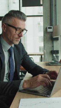 İki iş adamı parlak, modern bir ofiste dizüstü bilgisayarlara odaklandı. Takım elbiseli bir adam ve beyaz bluzlu bir kadın masada evraklar ve kahve fincanlarıyla yan yana çalışıyorlar..