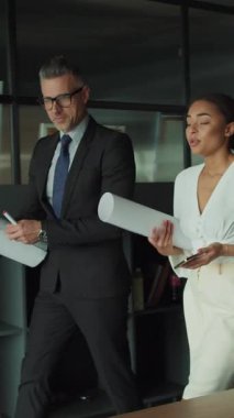 Resmi giyinmiş bir işadamı ve iş kadını modern bir ofiste büyük bir mimari planı inceliyor. Profesyonel işbirliği ve takım çalışması kavramı.