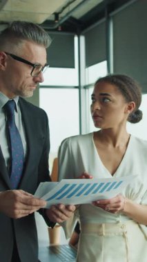 Modern bir ofiste çalışan bir işadamı ve iş kadını, finansal verileri kağıt üzerinde gözden geçirir, strateji ve analizlere dikkatle odaklanır..