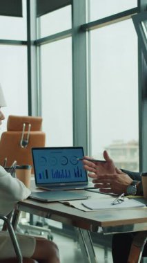 İşadamı, modern yüksek katlı bir ofiste dizüstü bilgisayarlı ve kahveli odaklı bir toplantı sırasında, pano kullanan bir bayan meslektaşına mali hat çizelgesini açıklıyor..