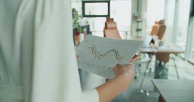 Bir iş kadını, modern bir ofisteki erkek arkadaşına basılı bir mali tablo gösterir. İş adamı kablosuz bir klavyede yazarken verileri gözden geçiriyor. 