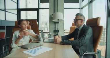 İki iş adamı modern bir ofiste kahve molası sırasında tesadüfen sohbet ederler. Dizüstü bilgisayarlar, grafikler ve gevşek ifadeler işbirlikçi bir ortamı vurgular.