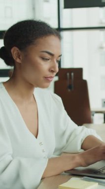 Genç iş kadını dizüstü bilgisayarla çalışırken, iş adamı arka planda bir şeyler yazıyor. Geniş pencereleri ve doğal ışığı olan modern ofis parlak bir atmosfer yaratıyor..