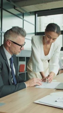 Genç iş kadını, modern bir ofiste profesyonel bir toplantı sırasında meslektaşına veri sunmak için masaya eğiliyor. Analiz ve işbirliğine odaklanıyorlar..