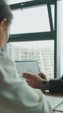 İşadamı, modern yüksek katlı bir ofiste dizüstü bilgisayarlı ve kahveli odaklı bir toplantı sırasında, pano kullanan bir bayan meslektaşına mali hat çizelgesini açıklıyor..