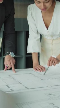 Profesyonel işadamı ve iş kadını modern ofis ortamında bir masada mimari planları tartışıyor, proje planlama ve tasarım stratejisine odaklanıyor.