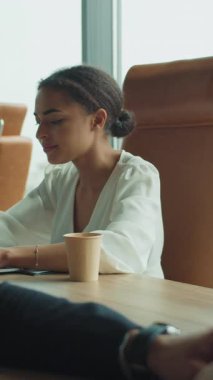 Parlak, modern bir ofiste dizüstü bilgisayara odaklanmış iş kadını tipleri, ön planda ise erkek bir meslektaşın biraz dikkati dağınık. Kahve fincanı ve şehir manzarası sahneyi tamamlar..