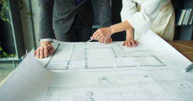 Bir iş adamı ve iş kadınının modern bir ofisin mimari veya tasarım projesinde işbirliği yaparak büyük bir planının kat planlarına işaret ettiği yakın plan.