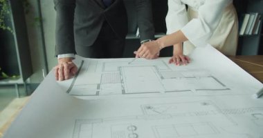 Bir iş adamı ve iş kadınının modern bir ofisin mimari veya tasarım projesinde işbirliği yaparak büyük bir planının kat planlarına işaret ettiği yakın plan.