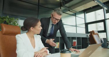 İş adamı, modern bir ofiste oturan bir iş kadınına bir rapor sunuyor. Takım iletişimi ve strateji planlaması devam ediyor.