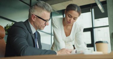 Kendine güvenen bir iş kadını profesyonel bir toplantıda erkek meslektaşına verileri açıklamak için masaya yaslanıyor. Modern ofis ortamında işbirliği ve takım çalışması.