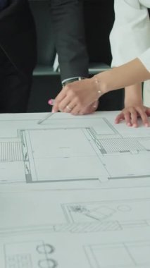 Bir iş adamı ve iş kadınının modern bir ofisin mimari veya tasarım projesinde işbirliği yaparak büyük bir planının kat planlarına işaret ettiği yakın plan.