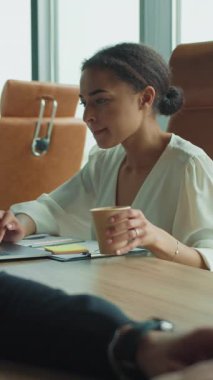 Kendine güveni tam bir iş kadını dizüstü bilgisayarında elinde bir fincan kahveyle, açık modern bir ofiste erkek bir iş arkadaşının yanında oturuyor. Büyük pencerelerden gün ışığı akışı.