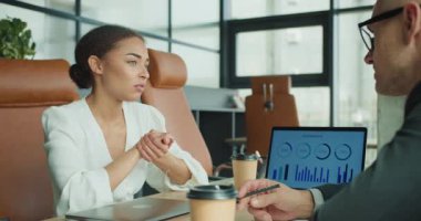 Modern bir ofiste kahve içerken sohbet eden iki iş adamı. Bir dizüstü bilgisayar ekranı stratejik tartışmaları sırasında bilgi verilerini görüntüler.