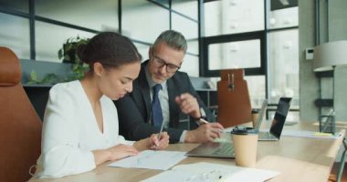 İş kadını ve işadamı, modern bir ofiste yapılan toplantı sırasında basılı veri tablolarını analiz etmeye odaklanarak, yakınlarda dizüstü bilgisayarlar ve kahve ile strateji üzerinde işbirliği yapıyorlar..