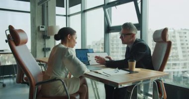 İş adamı ve iş kadını, bir toplantı sırasında veri ve plan stratejisini analiz etmek için bir dosya ve dizüstü bilgisayar kullanarak, modern bir ofiste mali tabloları birlikte gözden geçirirler..