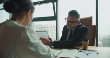 İşadamı, modern bir ofisteki bir toplantıda iş arkadaşına basılı satış çizelgesini açıklıyor. Her ikisi de mali verilere ve stratejik planlamaya odaklanmış durumda..