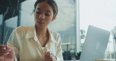 Modern bir ofiste dizüstü bilgisayar üzerinde çalışırken beyaz bluzlu genç bir iş kadını kalemle notlar yazar. İşine odaklanmış ve meşgul görünüyor. Yüksek kalite 4k görüntü