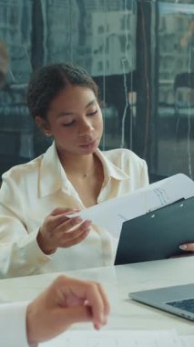 İş kadını, modern bir ofisteki bir toplantıda erkek meslektaşına verileri panoda sunar. Laptop ve evraklar beyaz masada görünüyor. Yüksek kalite 4k görüntü