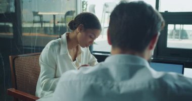 Bir iş kadını bir belgeye yazı yazarken bir erkek meslektaşı elinde dizüstü bilgisayarla karşıda oturuyor. Arka planda doğal ışık ve takım çalışması atmosferine sahip modern bir ofis ortamı görülebilir. Yüksek kalite