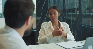 İş kadını, bir iş arkadaşına toplantıda iş stratejisini anlatırken el kol hareketi yapar. Modern ofis masasında bir kağıt ve bir dizüstü bilgisayar görünür. Yüksek kalite 4k görüntü