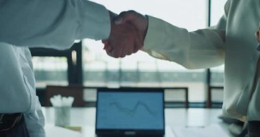 Ofis ortamında iş adamı ve iş kadınının el sıkışması. Finansal grafiği olan bir dizüstü bilgisayar arka planda, anlaşma, ortaklık ve takım çalışmasını sembolize ediyor. Yüksek