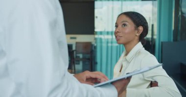 Modern ofis ortamında profesyonel bir kadın, erkek bir meslektaşını dikkatle dinliyor. Bir not panosundan bilgi sunuyor, iletişim ve liderlik becerilerini vurguluyor. Yüksek kalite 4k görüntü