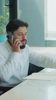 İş adamı telefonda konuşur ve notlar yazar. Bu sırada bir iş kadını dizüstü bilgisayarın yanındaki panoya bakar. Belgeler ve grafiklerle dolu modern bir ofis masasında oturuyorlar..