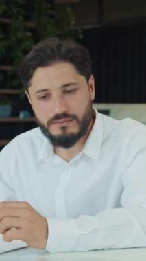 Beyaz gömlekli bir iş adamı toplantı sırasında bir meslektaşını dikkatle dinler. Modern bir ofis ortamında masanın üzerinde grafikli kağıtlar ve dizüstü bilgisayarlar görünür..