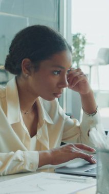 Parlak bir ofis masasında dizüstü bilgisayarda çalışan genç bir iş kadını, etrafındaki dokümanlar ve modern çalışma alanı unsurlarıyla verileri derinden inceliyor ve analiz ediyor..