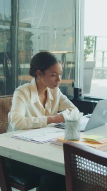 Odaklanmış iş kadını, parlak, modern bir ofiste tek başına oturuyor. Masasında belgeler ve kırtasiye kağıtları olan bir dizüstü bilgisayar üzerinde çalışıyor. Düşünce ve analizlerle dolu..