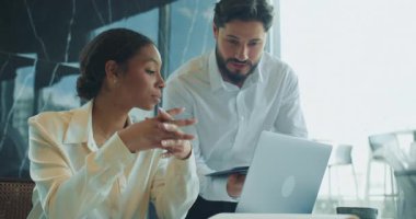 Bir iş kadını dizüstü bilgisayarla masada otururken, bir erkek meslektaşı da pano kullanarak fikir sunuyor. Parlak bir ofiste profesyonel bir tartışmayla meşgul görünüyorlar. Yüksek kalite 4k görüntü