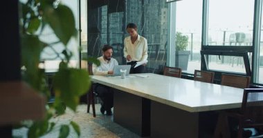 İş adamı elinde belgelerle gülen meslektaşı yanında dururken bir dizüstü bilgisayarda çalışıyor. Mermer masası ve pencereleri olan parlak ve modern bir ofiste iş birliği yapıyorlar. Yüksek kalite 4k görüntü