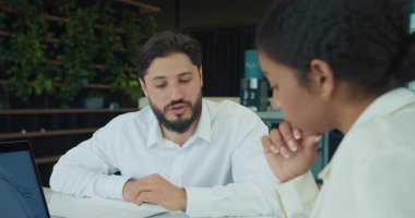 İş adamı, bir toplantıda meslektaşına bir şey açıklarken yazılı bir tablodaki verilere işaret ediyor. Grafikleri ve modern ofis geçmişi olan bir laptop görülebilir. Yüksek kalite 4k görüntü