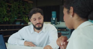 İş adamı bir ofis toplantısı sırasında iş arkadaşlarının fikirlerini dinlerken ilgiyle gülümser. Modern bir çalışma alanında dizüstü bilgisayar ve belgeler masanın üzerinde görünür. Yüksek kalite 4k görüntü