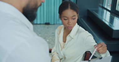 Bir iş kadını, bir iş arkadaşıyla iş yerinde yaptığı bir tartışmada elinde kalem tutarken bir belgeyi dikkatle inceliyor. Analiz üzerine odaklanmış profesyonel bir ortam. Yüksek kalite 4k görüntü