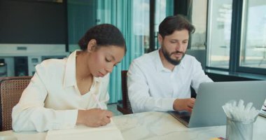 Bir iş adamı dizüstü bilgisayarda yazarken bir iş kadını onun yanına notlar yazıyor. Parlak ve modern bir ofis ortamında birlikte çalışıyorlar. Kahve fincanlarıyla birlikte. Yüksek kalite 4k görüntü