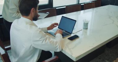 İşadamı, yanında telefon, belge ve kalem tutacağı olan modern bir mermer ofis masasında dizüstü bilgisayarda çalışıyor. Bir meslektaşı elinde raporla yanında duruyor. Yüksek kalite 4k görüntü