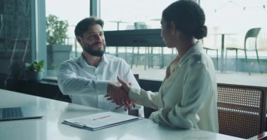 Bir işadamı ve bir iş kadını, modern bir ofisin masasında karşılıklı oturup bir belgeyi incelerken sohbet ediyorlar. Ayarlar takım çalışması ve planlama öneriyor. Yüksek