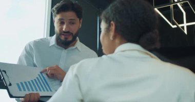 Bir işadamı, bir toplantı sırasında kadın meslektaşına modern bir ofis ortamındaki iş büyümesini vurgulayan bir bar tablosunu gösterir ve açıklar. Yüksek kalite 4k görüntü