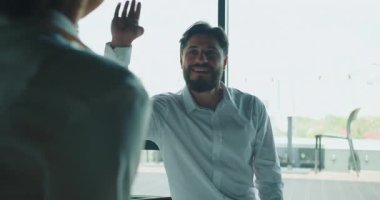 Gülümseyen işadamı modern ofis ortamında bir meslektaşına beşlik çakıyor. Bu jest takım çalışmasını, başarıyı, motivasyonu ve iş hayatında olumlu bir iş ilişkisini simgeliyor. Yüksek kalite 4k