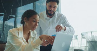 Bir işadamı ve iş kadını modern ofis ortamında dizüstü bilgisayardaki çizelge ve verileri analiz eder. Ekip toplantıları sırasında meşgul ve işbirlikçi görünüyor. Yüksek kalite 4k görüntü