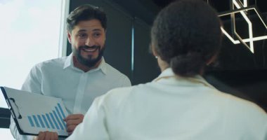 Bir iş adamı, modern bir ofisteki iş yerinde iş arkadaşına mavi çizelge gösteriyor. Ekip performans ve büyüme sonuçlarını tartışmaya odaklandı. Yüksek kalite 4k görüntü