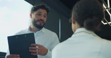 Beyaz gömlekli bir işadamı, ofis ortamındaki bir bayan meslektaşına bir pano gösterirken gülümsüyor ve olumlu ve işbirlikçi bir tartışma öneriyor. Yüksek kalite 4k görüntü