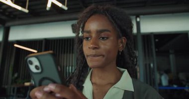 Odaklanmış ve konsantre bir kadın, modern bir ofis ortamında akıllı telefonuyla aktif olarak etkileşim içindedir.