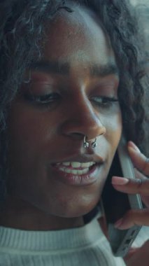 Kıvırcık saçlı ve burun halkalı bir kadın bir telefon konuşmasında duygularını yansıtıyor..